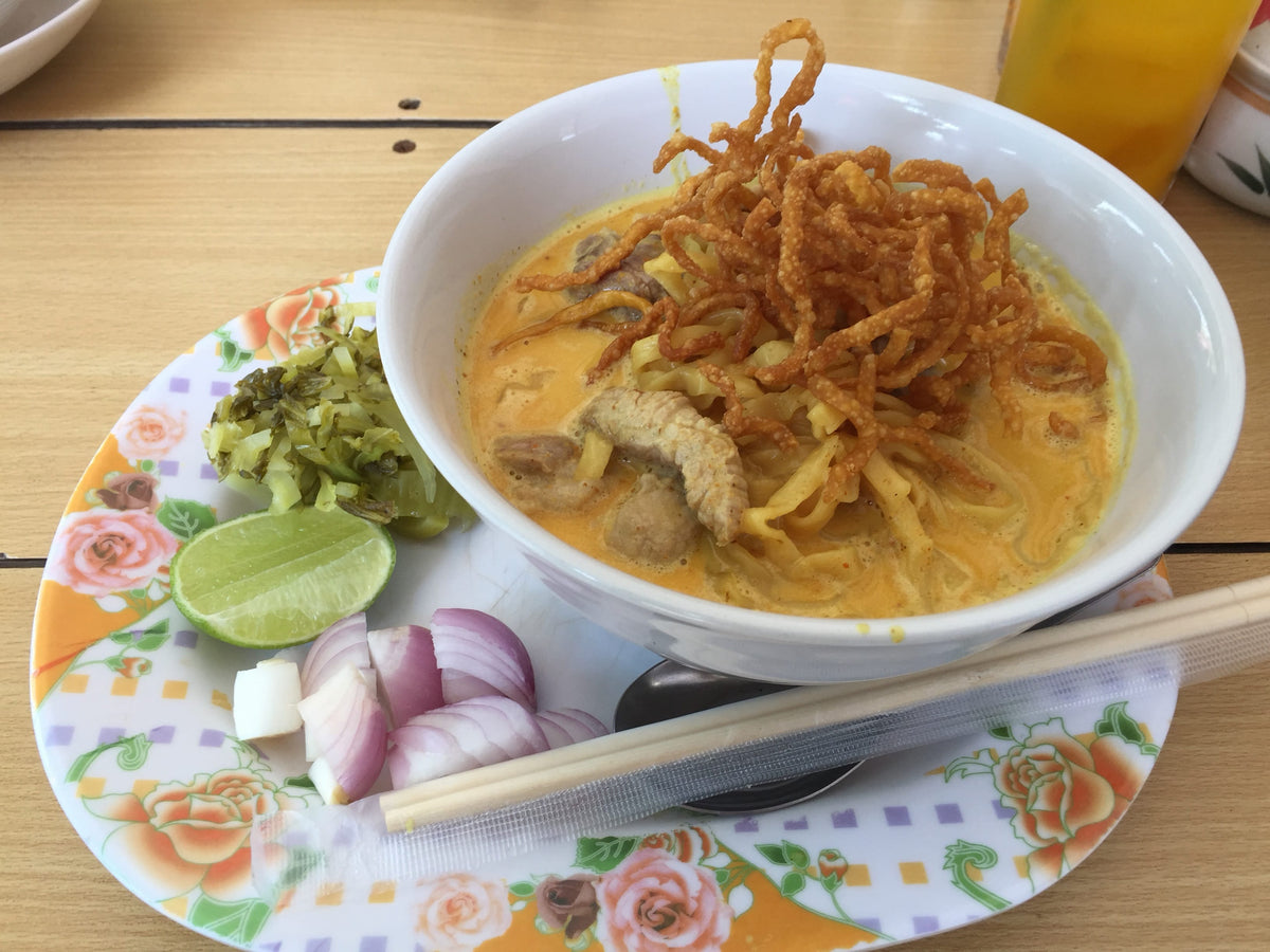 Bowl of northern Thai khao soi curry noodle soup with fried shallots, pickled mustard greens, red onion, and lime